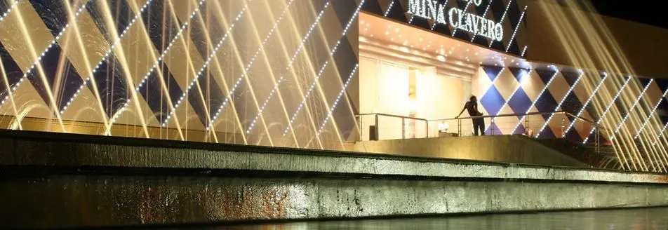 Casino Mina Clavero at night, its name over the entrance and lit water jets in front of the diamond-patterned facade — Casino Mina Clavero